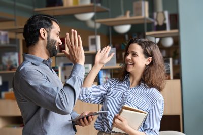 Two happy friendly diverse professionals, teacher and student giving high five standing in office celebrating success, good cooperation result, partnership teamwork and team motivation in office work.